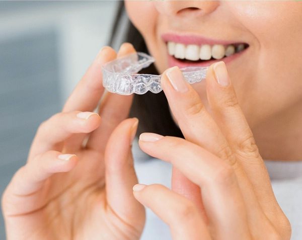 Clear dental aligner held in front of a smile